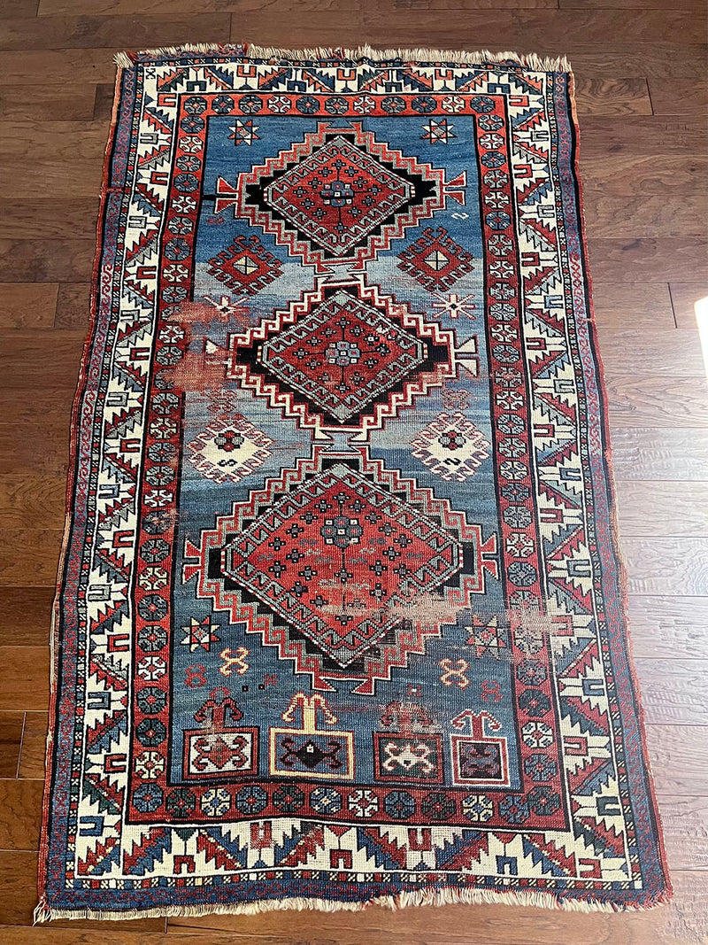 an antique caucasian rug with a blue field with faded red medallions