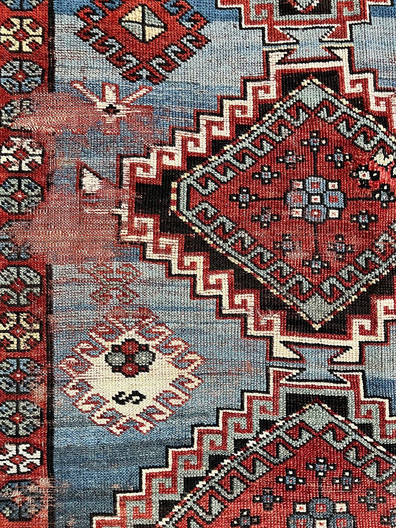 an antique caucasian rug with a blue field with faded red medallions