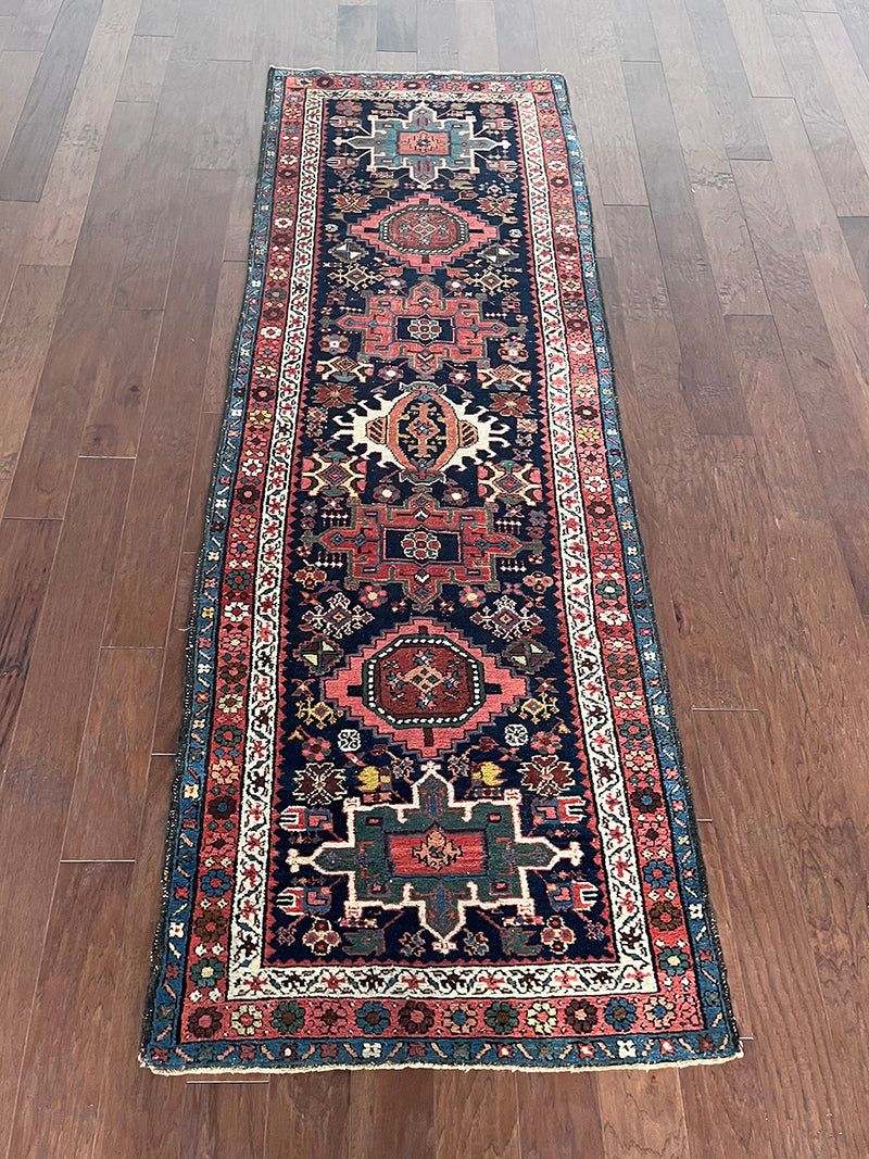 an antique heriz karajah runner with a dark blue field and pink and teal medallions