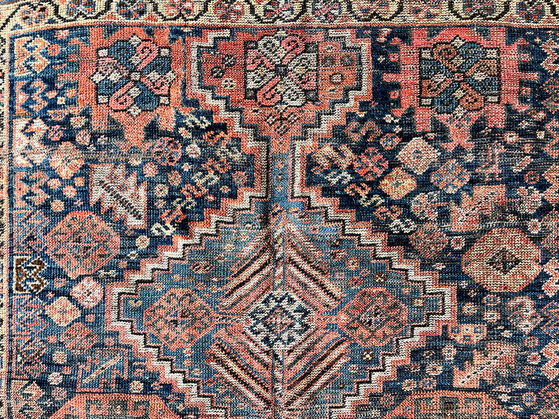 an antique shiraz qashqai rug with a dark blue field and brick red medallions