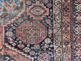 an antique shiraz qashqai rug with a dark blue field and brick red medallions