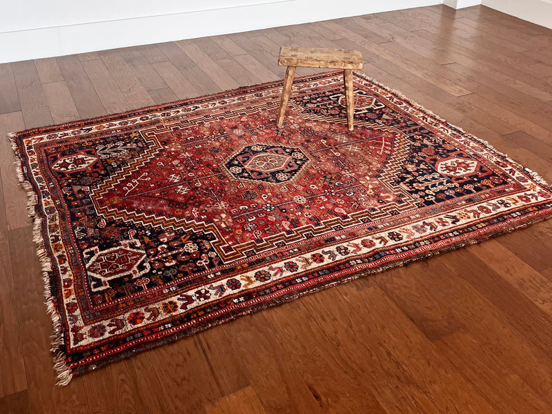 a vintage qashqai rug with a red palette and dark blue corners 
