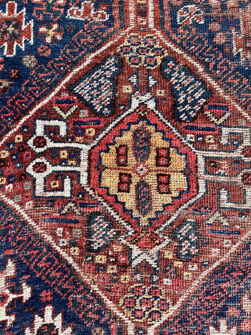 an antique shiraz qashqai rug with red accents and a dark blue field