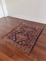 an antique shiraz qashqai rug with red accents and a dark blue field