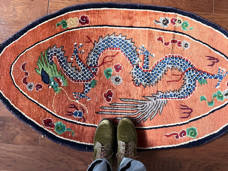 an antique oval-shaped chinese rug with an orange field and a four-clawed dragon motif