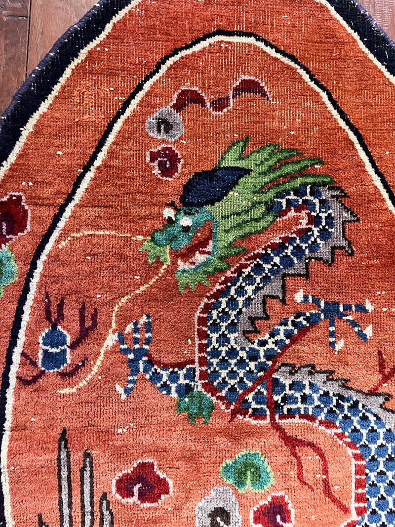 an antique oval-shaped chinese rug with an orange field and a four-clawed dragon motif