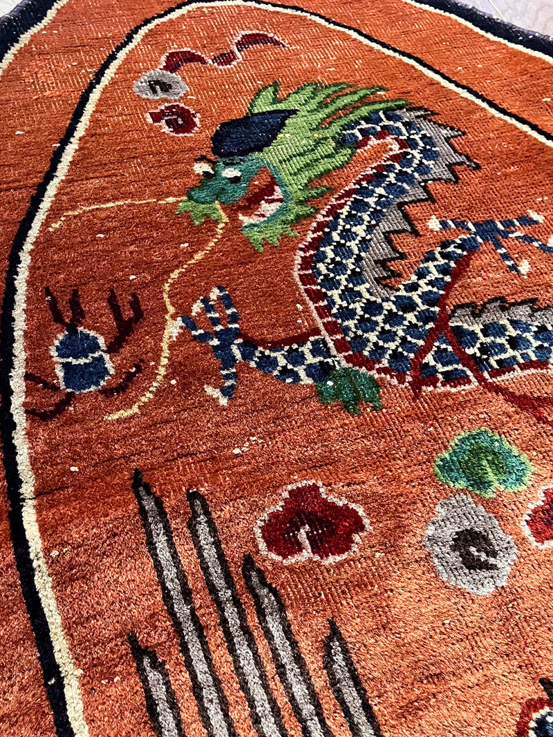 an antique oval-shaped chinese rug with an orange field and a four-clawed dragon motif