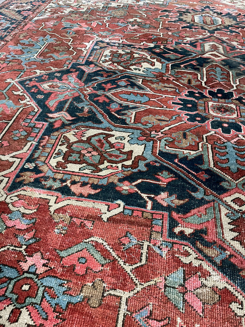 an antique heriz rug with a rusty red field and large navy blue medallion