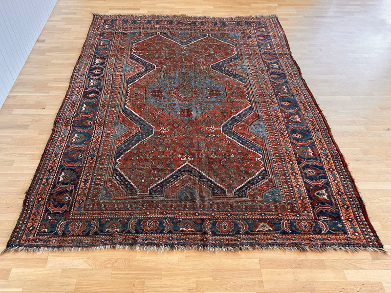 a large antique qashqai rug with a terracotta field and blue accents