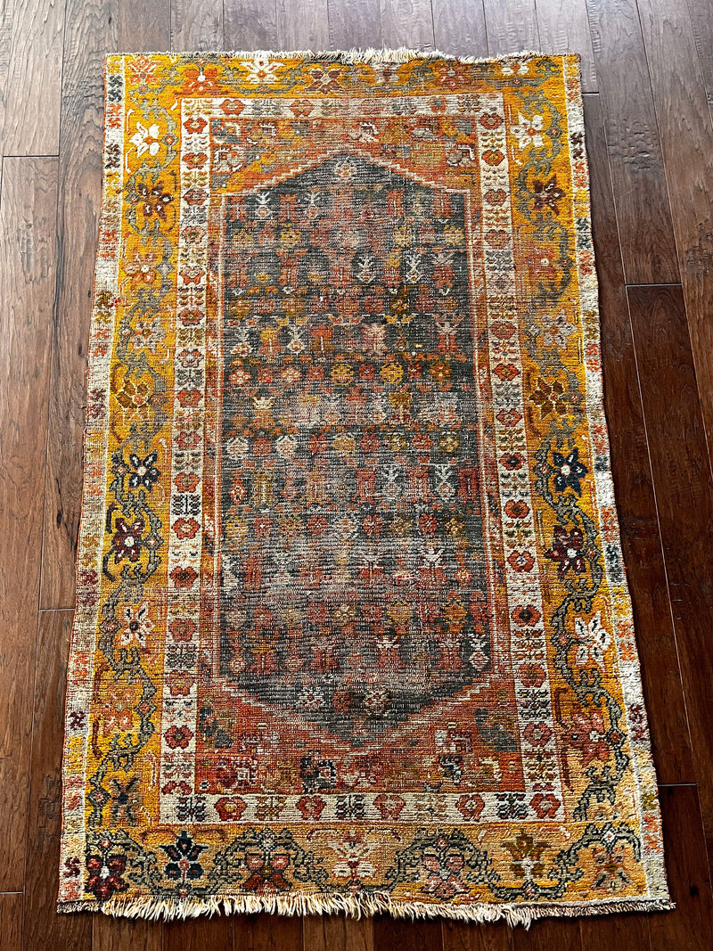 an antique oushak rug with a yellow border and grey field 