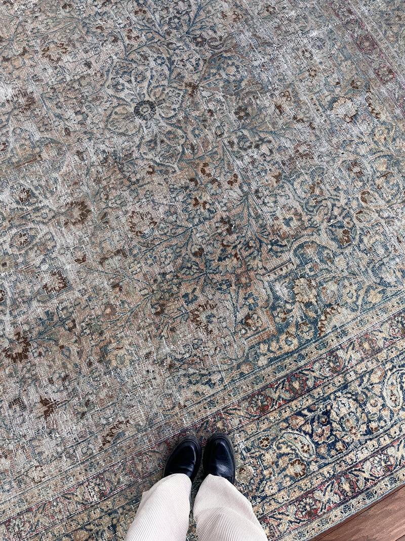 a vintage faded mashad rug with blue and brown floral accents on a beige field