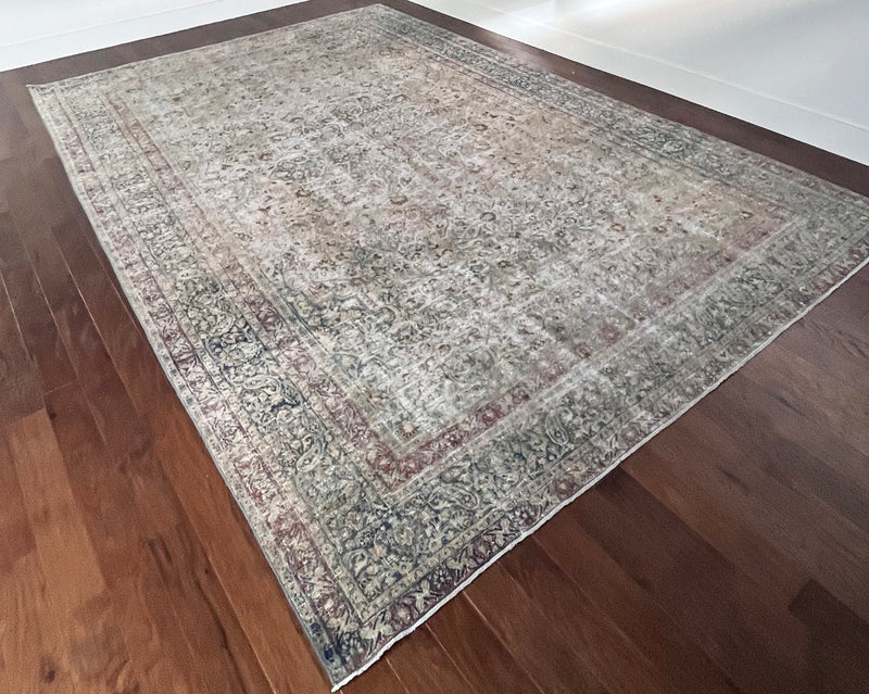 a vintage faded mashad rug with blue and brown floral accents on a beige field