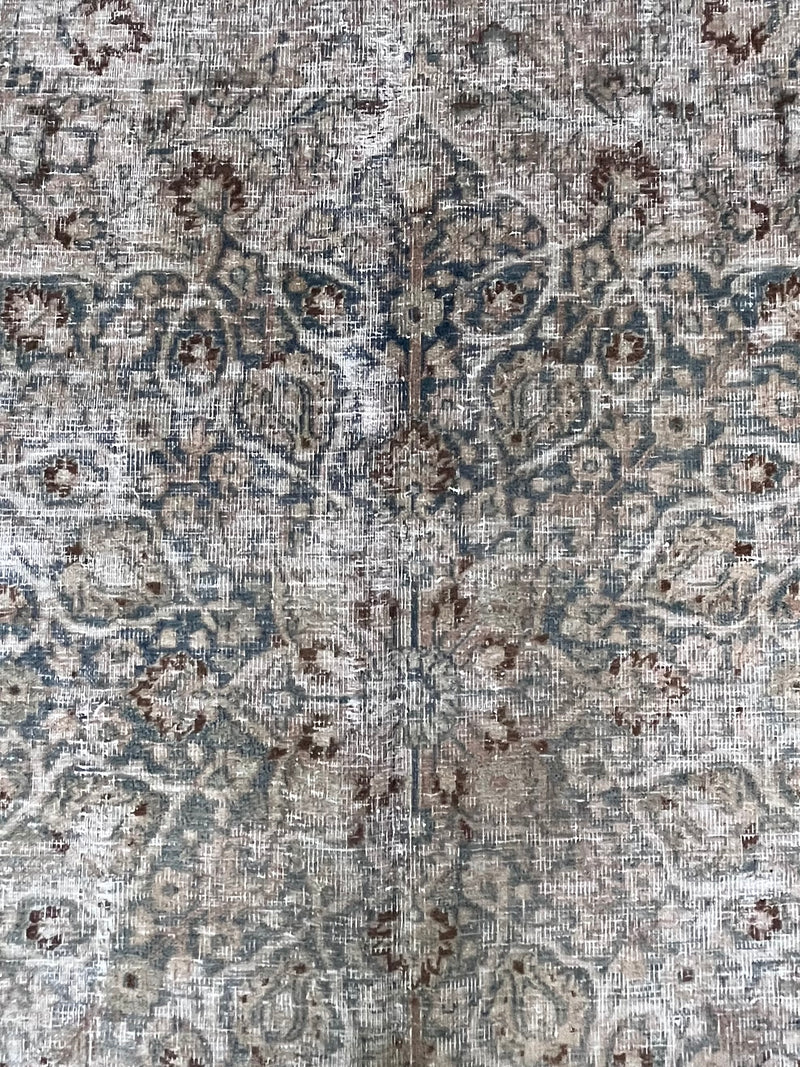a vintage faded mashad rug with blue and brown floral accents on a beige field