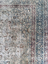 a vintage faded mashad rug with blue and brown floral accents on a beige field