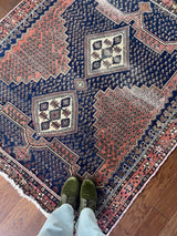 A vintage Afshar rug with a coral field and paisley on a navy background.