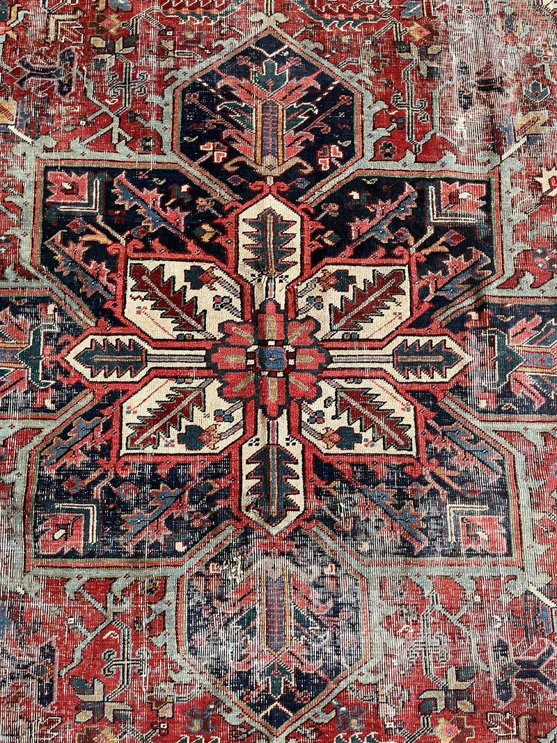 a large antique heriz rug with a red field and blue, pink, coral and green accents and intricate floral details