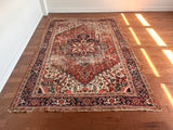 a large antique heriz rug with a red field and blue, pink, coral and green accents and intricate floral details