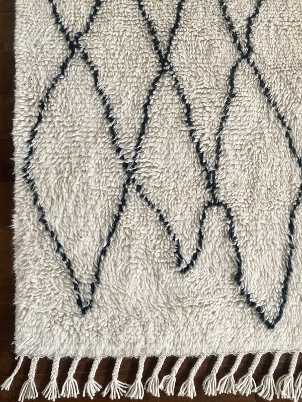 a vintage berber rug with uneven black diamond pattern on a cream field