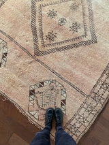 a vintage moroccan rug with brown geometric accents on a soft salmon pink field