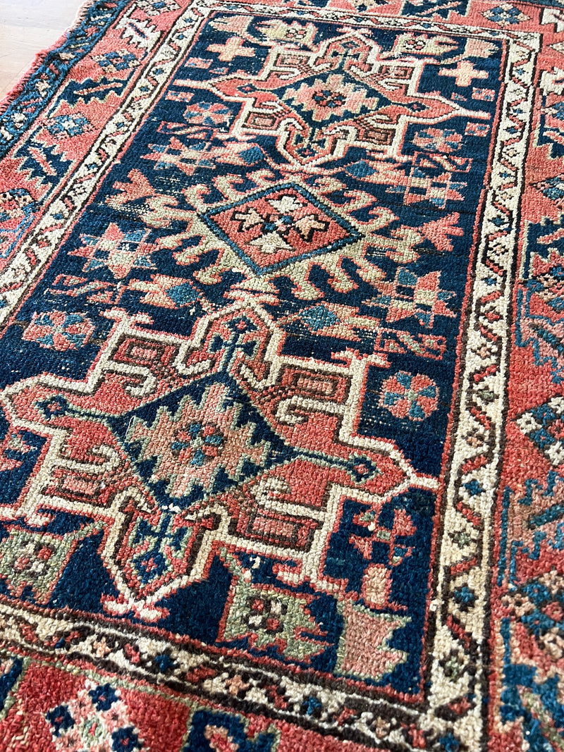 a mini heriz rug with a navy blue field and coral accents