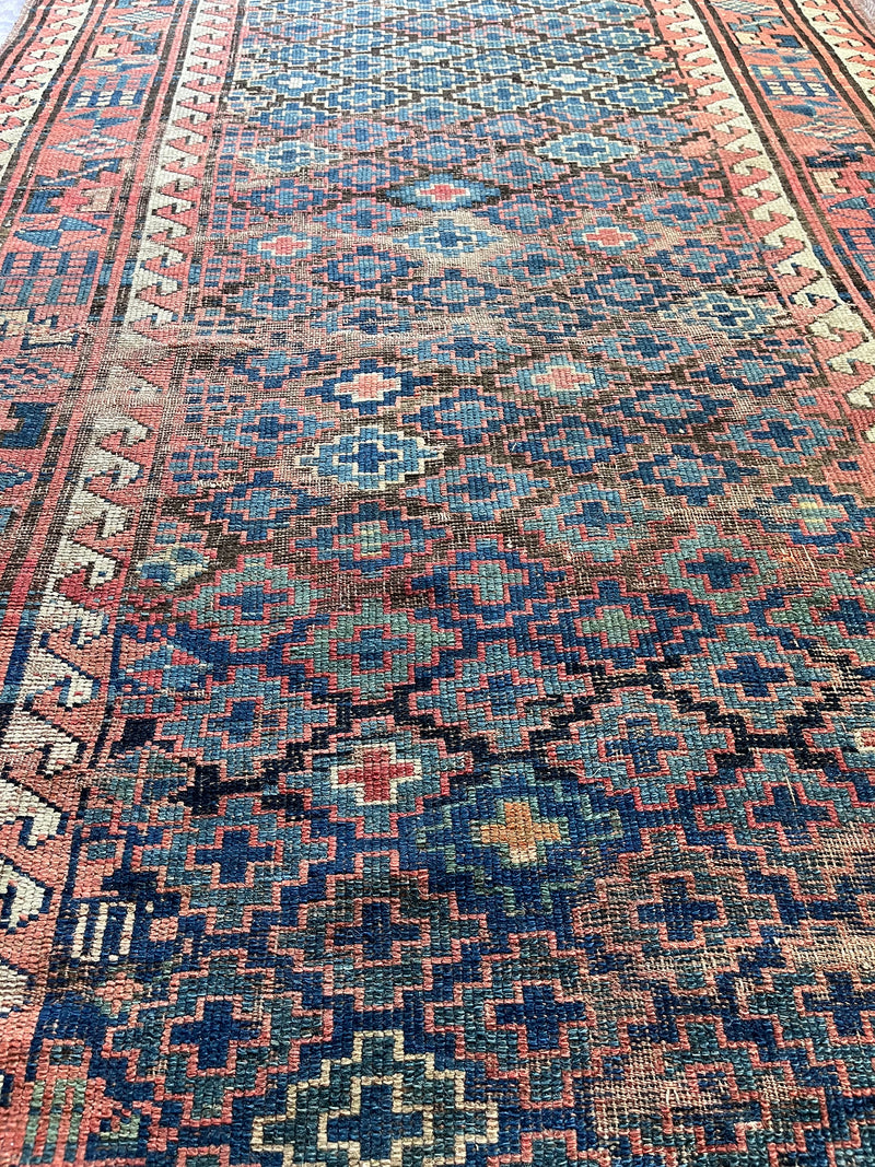 an antique kazak rug with pretty coral accents and a diamond pattern on a blue field