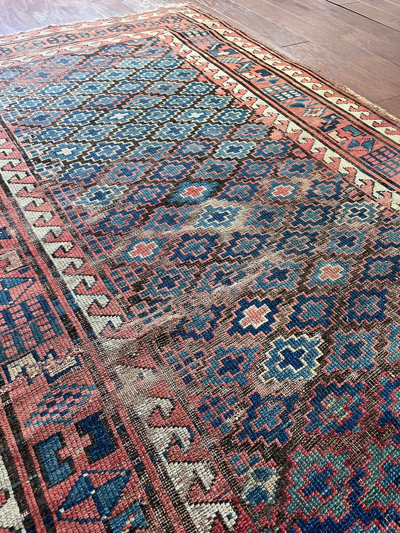 an antique kazak rug with pretty coral accents and a diamond pattern on a blue field