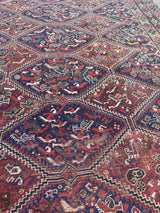 a large antique qashqai rug with a dark blue field, animal motifs and earthy accents
