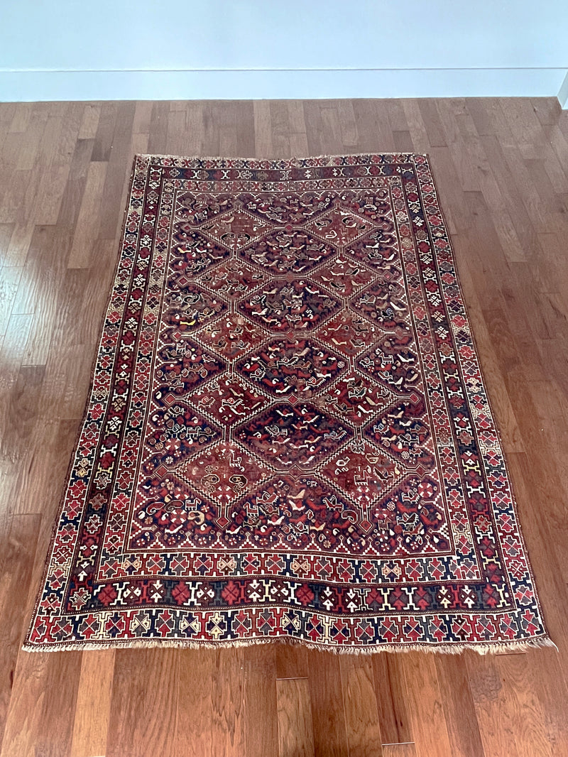 a large antique qashqai rug with a dark blue field, animal motifs and earthy accents