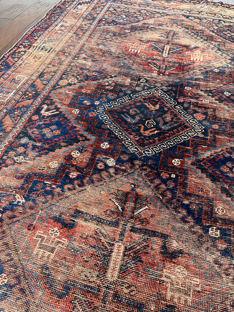 an antique shiraz rug with a coral, navy and red palette