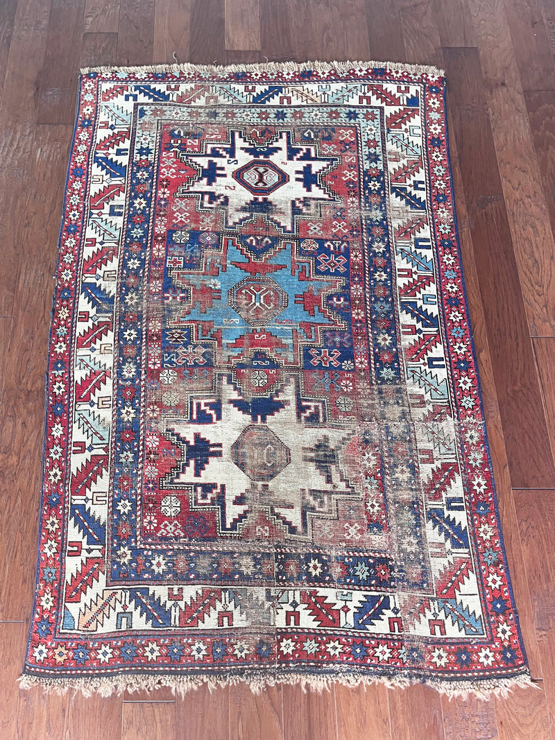 an antique caucasian rug with red and blue accents and a large geometric pattern