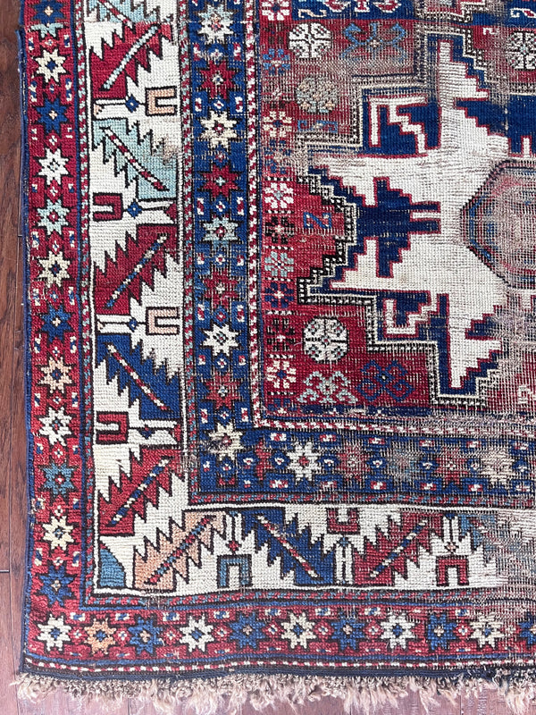 an antique caucasian rug with red and blue accents and a large geometric pattern